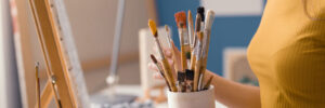 Young female artist holding brushes and choosing the right one for her work, art supplies and creativity concept