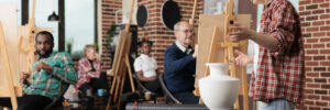 Group of diverse people learn how to draw realistic items, listening teacher and drawing on canvas. Family involved in art activity spending time together. Creative leisure activities for adults